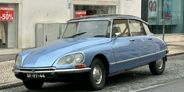 pexels-photo-30344009-30344009 Vintage Citroën DS car parked on cobblestone street with promotional sale signs in the backdrop.